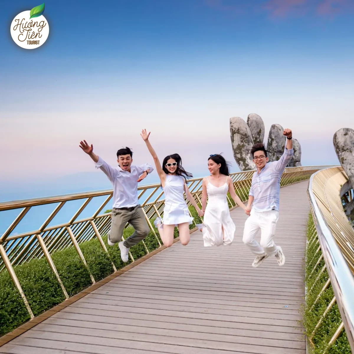 Friends jumping with joy on the Golden Bridge in Da Nang, Vietnam, with stunning mountainous background.