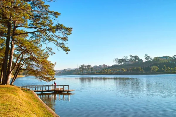 The calm waters of Xuan Huong Lake surrounded by autumn foliage and a wooden dock.