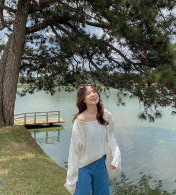 A tourist smiling under pine trees with a view of Xuan Huong Lake in Dalat.